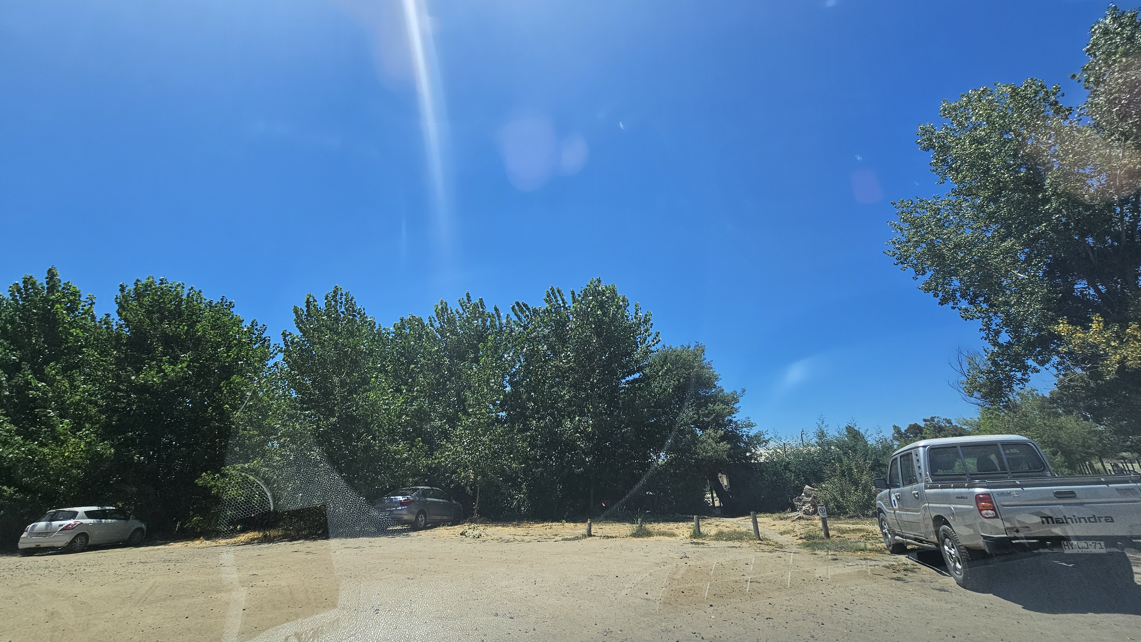 Fotografía del estacionamiento del parque que cuenta con suelo de tierra, es amplio y se aprecian vehículos estacionados